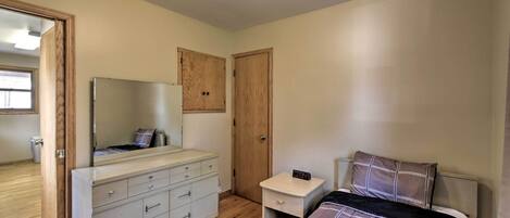 A bedroom with a bed, a dresser, a nightstand, a mirror, and two doors.