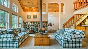 A spacious living room with two checkered sofas, a wooden coffee table, a stone fireplace, and a staircase leading to an upper level. - Hot Tub Access, Near Skiing: Tahoe Donner Cabin (Truckee)