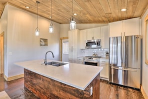 Una cocina con una isla central, electrodomésticos de acero inoxidable, techo de madera e iluminación colgante.
