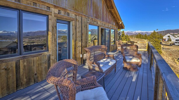 Une terrasse en bois, meublée de meubles en osier, et de grandes fenêtres donnant sur un paysage montagneux.