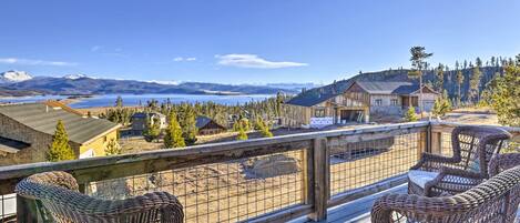 A wooden deck with wicker chairs overlooking a lake and mountains.