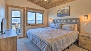 Une chambre dotée d’un grand lit, d’un ventilateur de plafond, d’une tête de lit en bois, d’une fenêtre donnant sur les montagnes et d’un bureau avec un ordinateur.