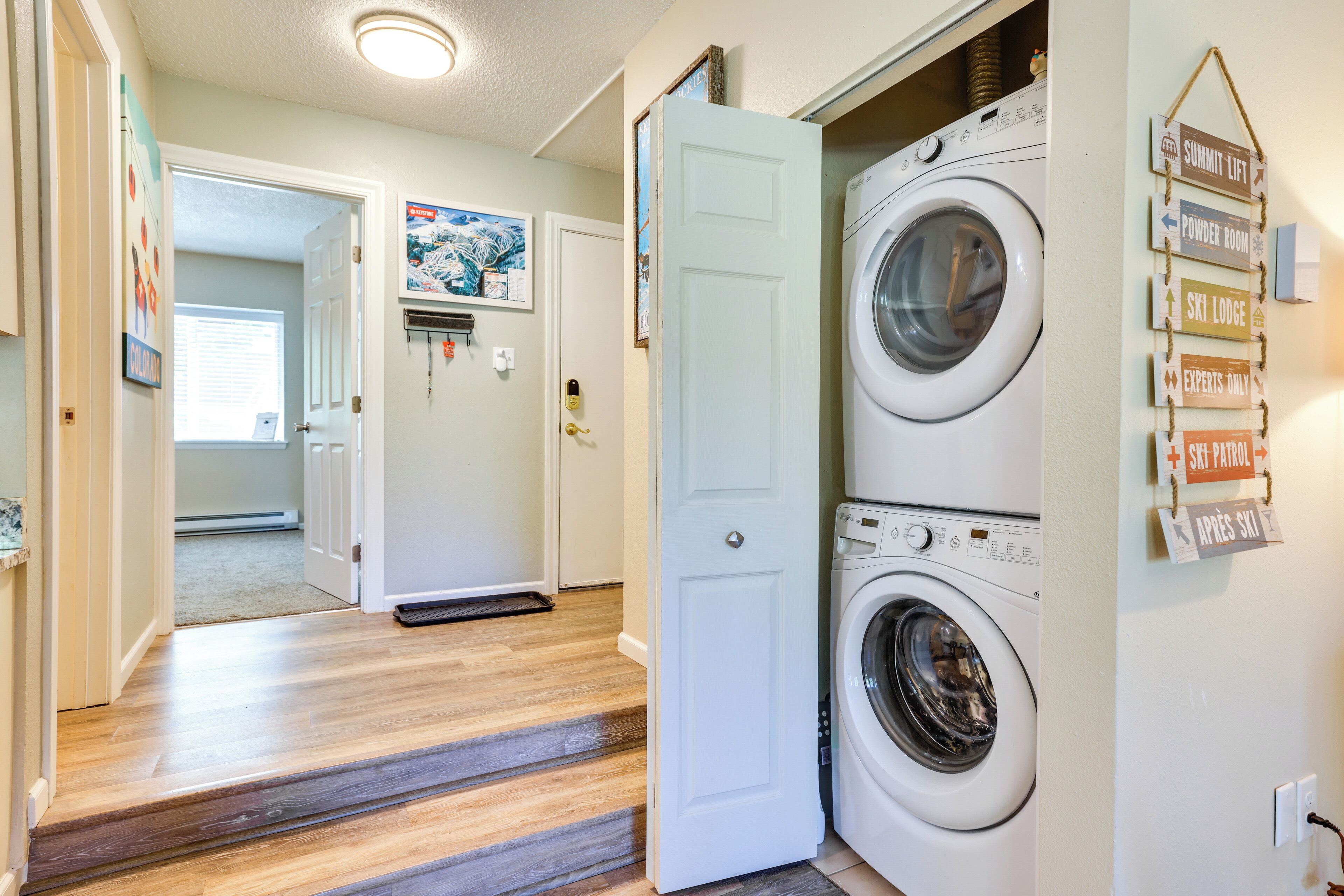 A laundry room with a washing machine and dryer, a door leading to another room, and a sign indicating a ski lodge.