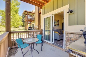 Une terrasse extérieure avec une table et des chaises, un barbecue et une porte-fenêtre coulissante donnant sur un espace de vie comprenant un canapé et un tableau.