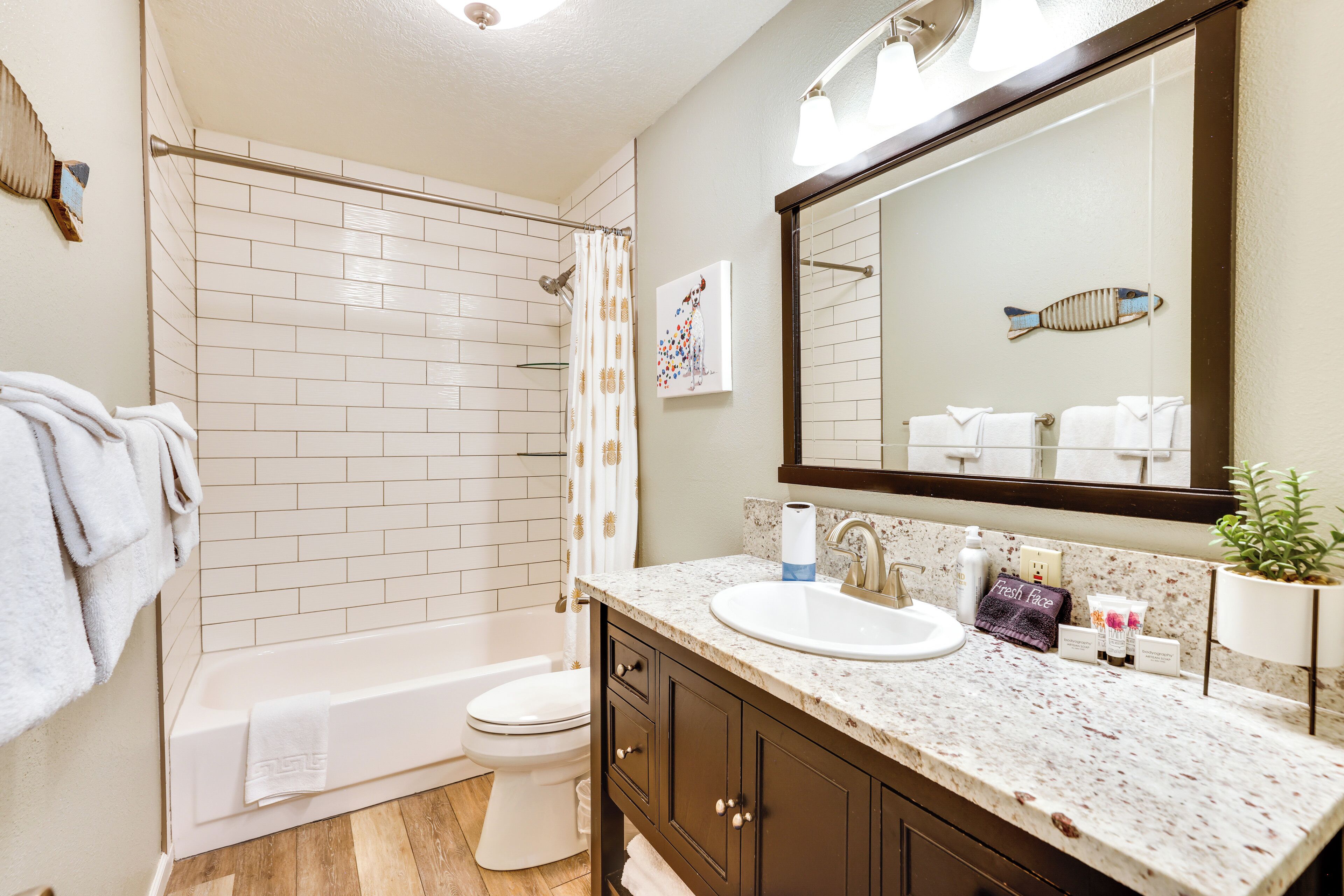 A modern bathroom with a white bathtub, a toilet, a sink with a marble countertop, and a large mirror.