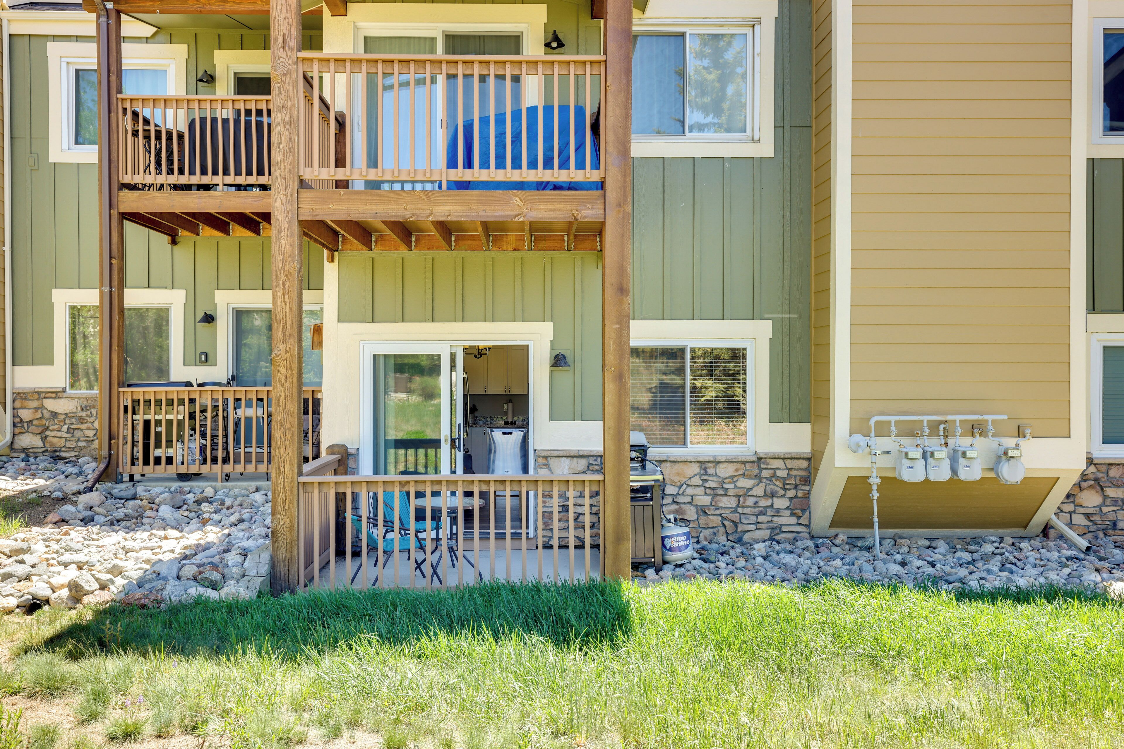 A multi-story residential building with a wooden deck, outdoor seating, and a stone foundation.