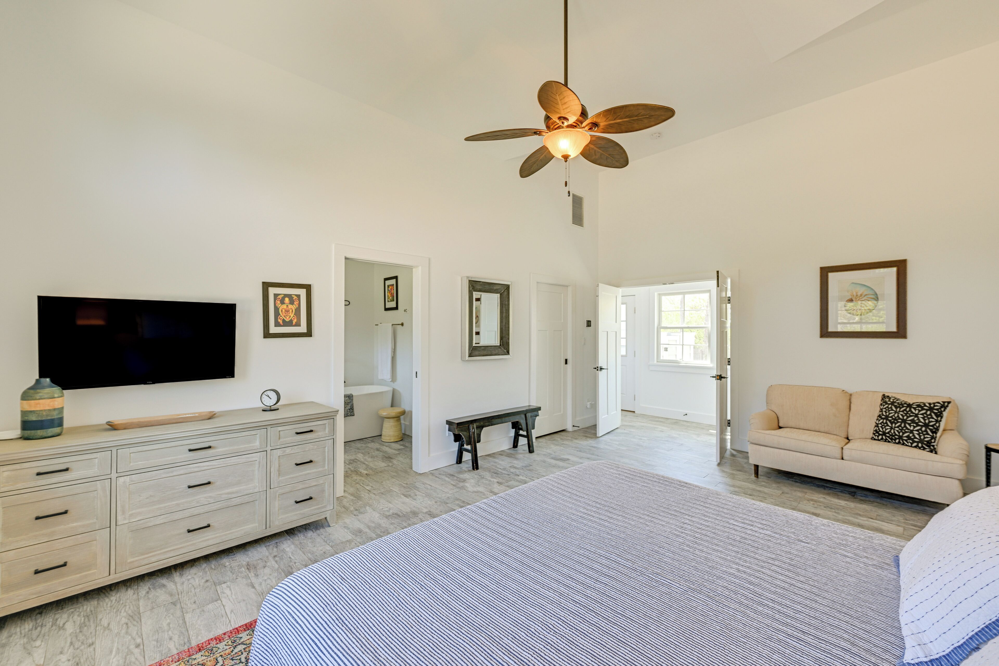 A spacious bedroom with a large bed, a television, a ceiling fan, and a view into the bathroom.