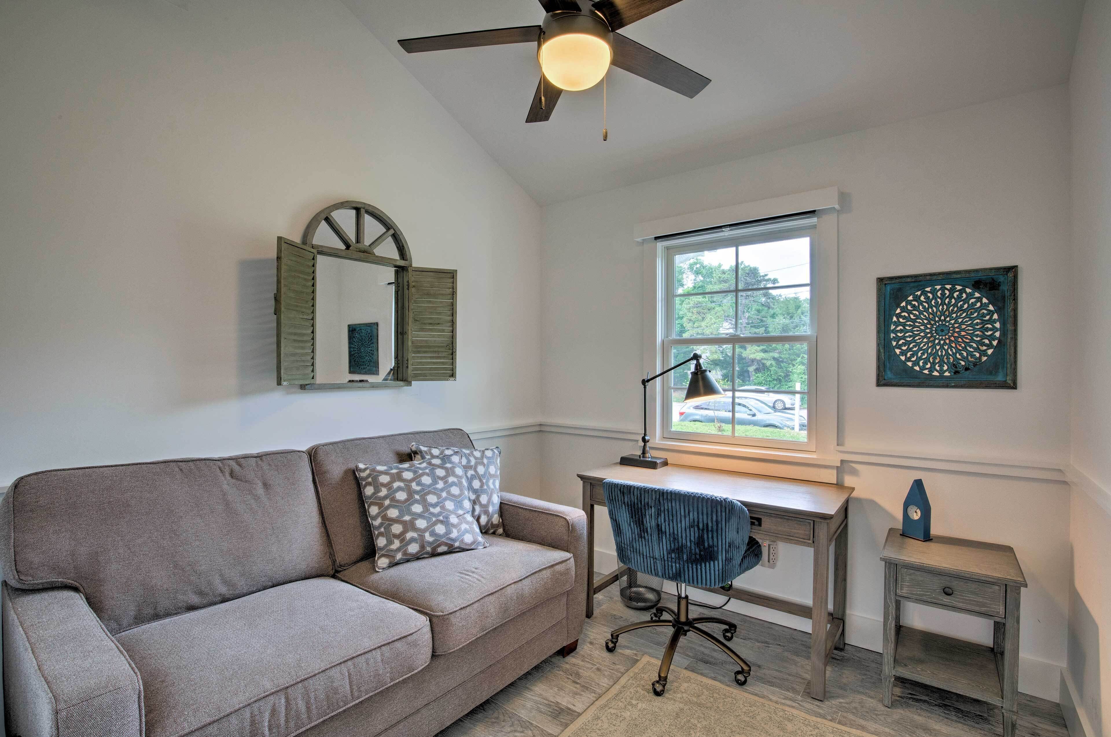 A room with a sofa, desk, chair, and a small table.