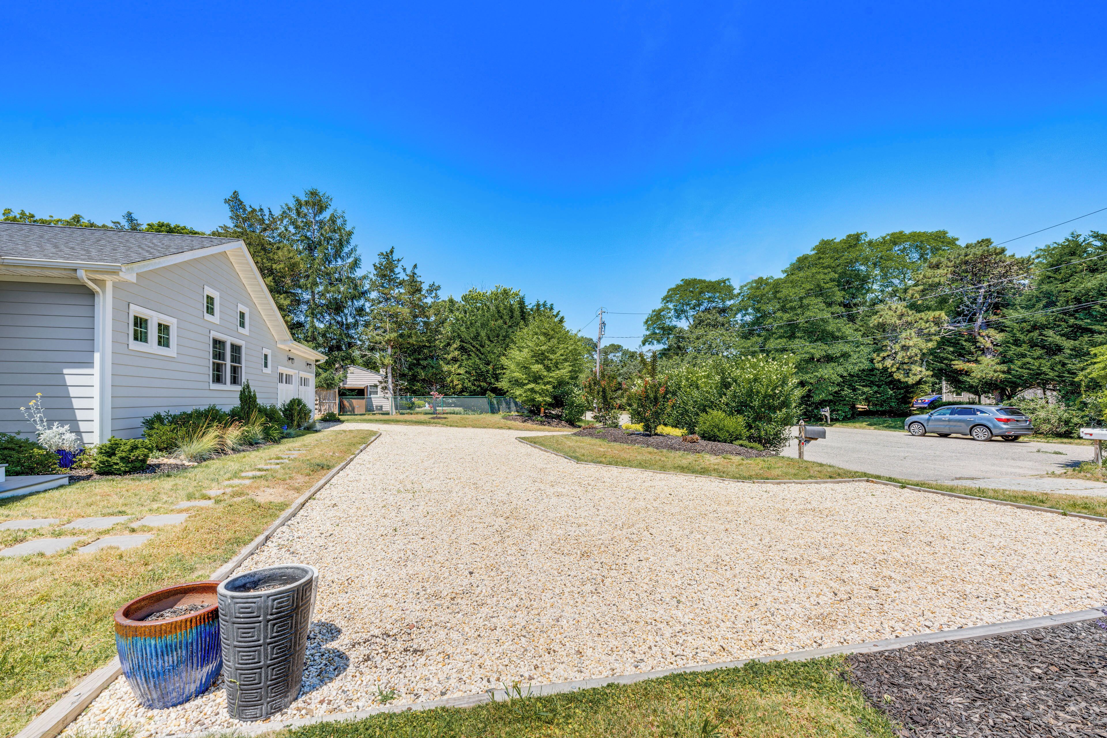 A residential driveway with gravel, a house on the left, and a car parked on the street.