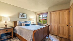 Une chambre à coucher avec un lit en bois, des tables de chevet, une fenêtre donnant sur un beau paysage et une armoire en bois.