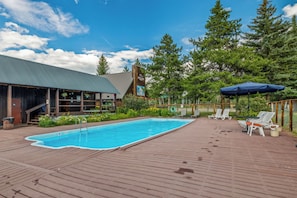 Un espace piscine doté d’une terrasse en bois, de chaises longues et d’un coin salon abrité.