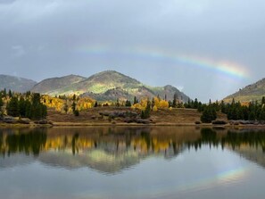 A calm lake with a reflection of trees and mountains, a rainbow, and a cloudy sky. - Knapsack- Mountain cabin with beautiful views (Clark)