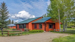 A red cabin with a green roof, surrounded by trees and a gravel path. - Knapsack- Newly updated mountain cabin! (Clark)