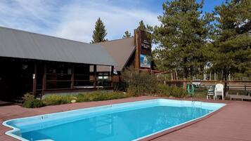 A swimming pool with a wooden deck, a building with a sign, and trees in the background.