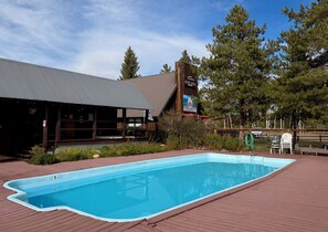 A swimming pool with a wooden deck, a building with a sign, and trees in the background. - Knapsack- Newly updated mountain cabin! (Clark)