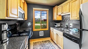 A kitchen with wooden cabinets, a microwave, a stove, a refrigerator, and a window with a view of the outside. - Knapsack- Newly updated mountain cabin! (Clark)