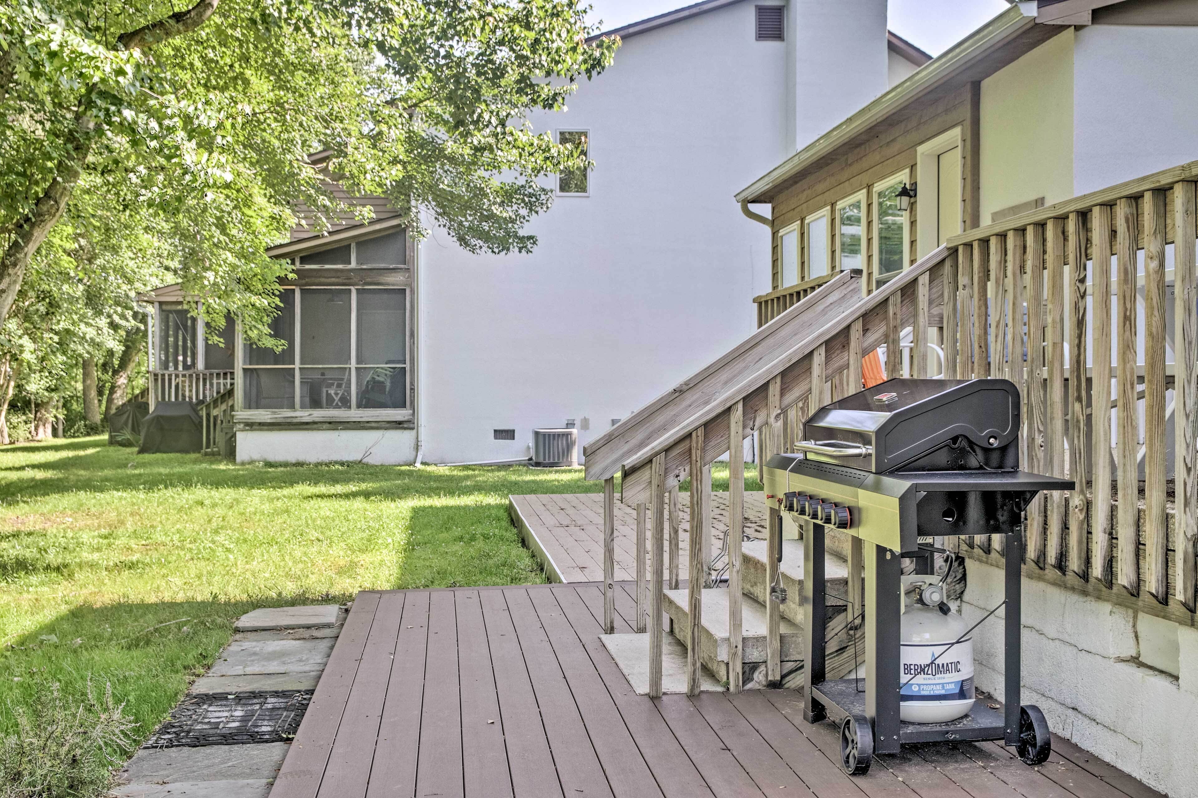 A backyard with a wooden deck, a grill, and a propane tank.