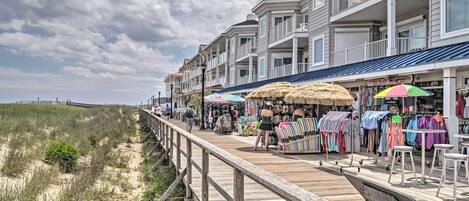 A wooden boardwalk with shops and a beach in the background.