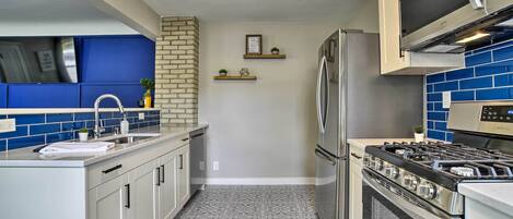 A kitchen with a stainless steel refrigerator, a built-in oven, and a microwave. There are two shelves with potted plants and a framed picture on the wall.