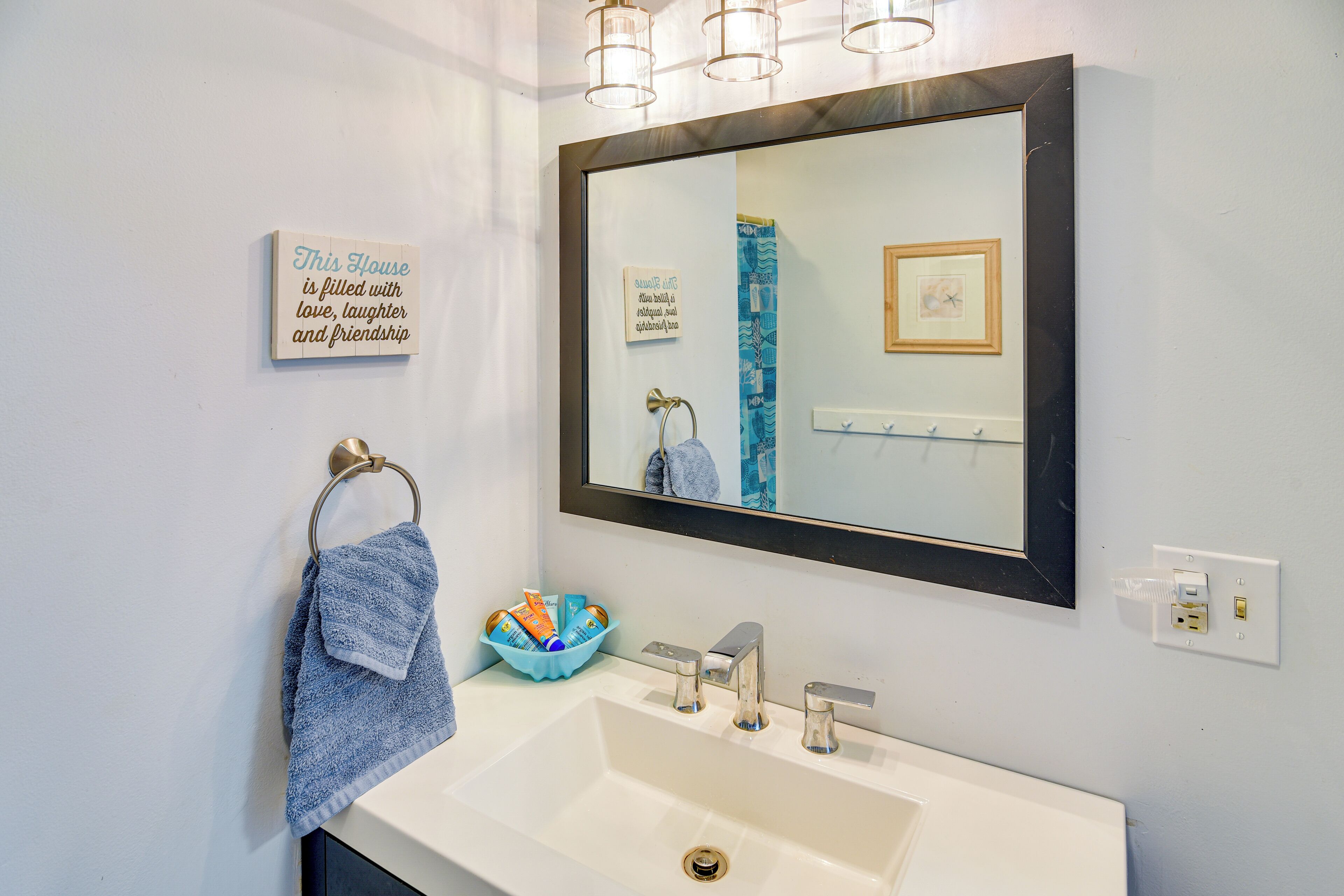 A bathroom with a white sink, a mirror, and a towel rack. There is a sign on the wall and a blue towel hanging on the rack.