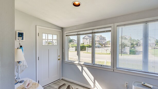 A room with a white door, a window with blinds, a lamp, a small table with a decorative item, and a radiator. - Quaint Coastal Cottage With Patio! (Charlestown)