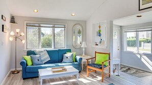A living room with a blue sofa, a white coffee table, a wooden chair, and a large window providing natural light.