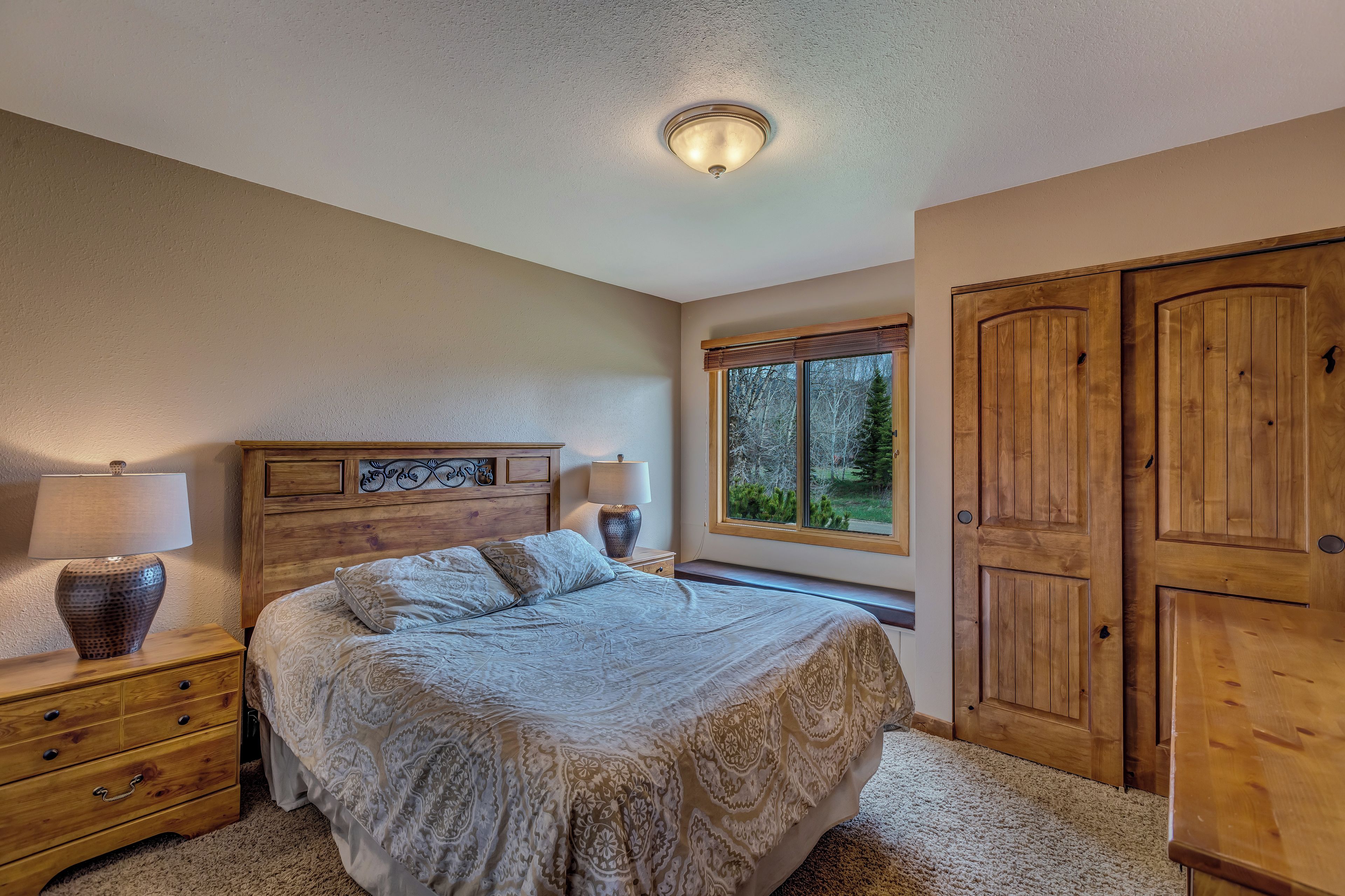 Une chambre avec un grand lit, une armoire en bois et une fenêtre donnant sur les arbres.