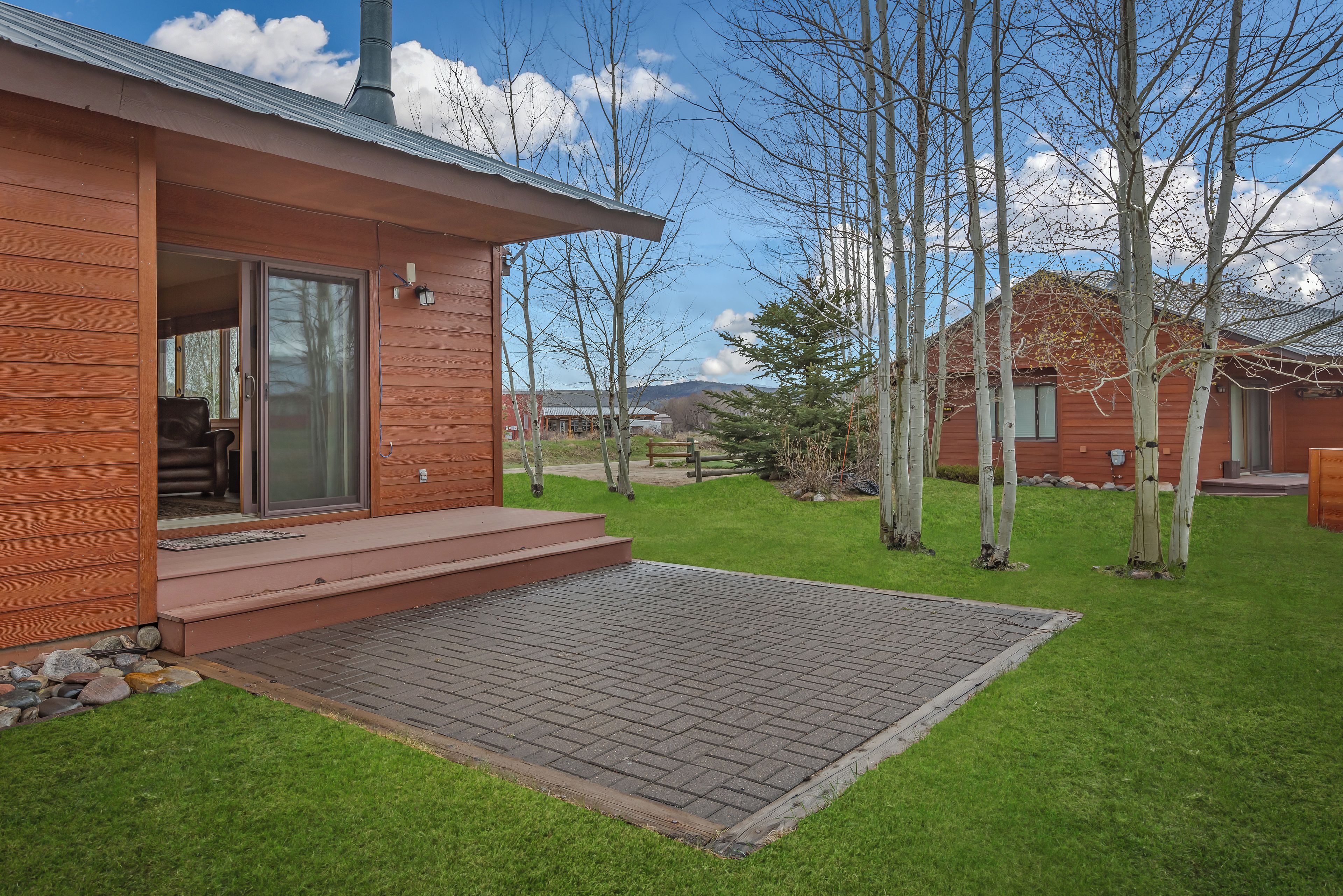 Une cabane moderne en bois, dotée d’un patio, d’une porte-fenêtre coulissante et offrant une vue sur une montagne en arrière-plan.