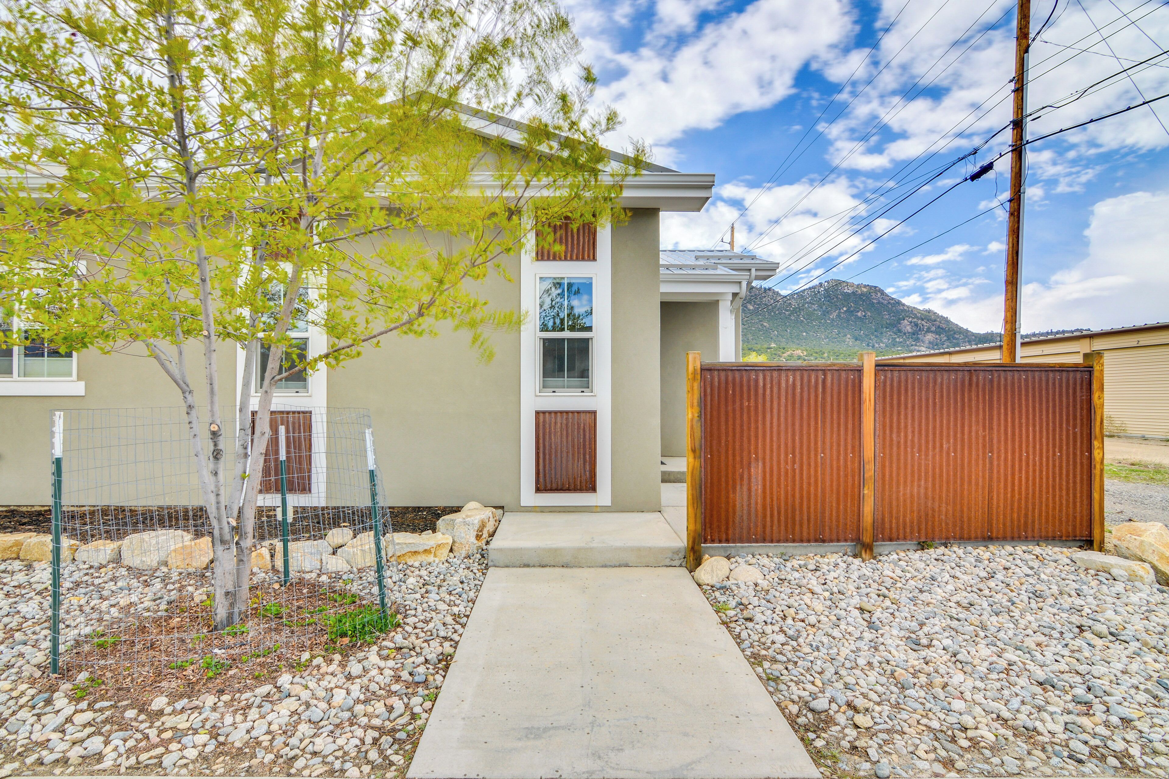 A modern house with a concrete pathway leading to the entrance, surrounded by a wooden fence and a small tree.