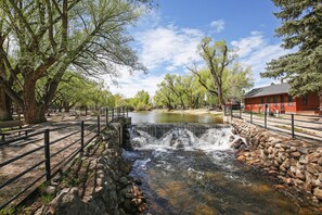 A small waterfall in a park with a stone wall, trees, and a red building in the background.