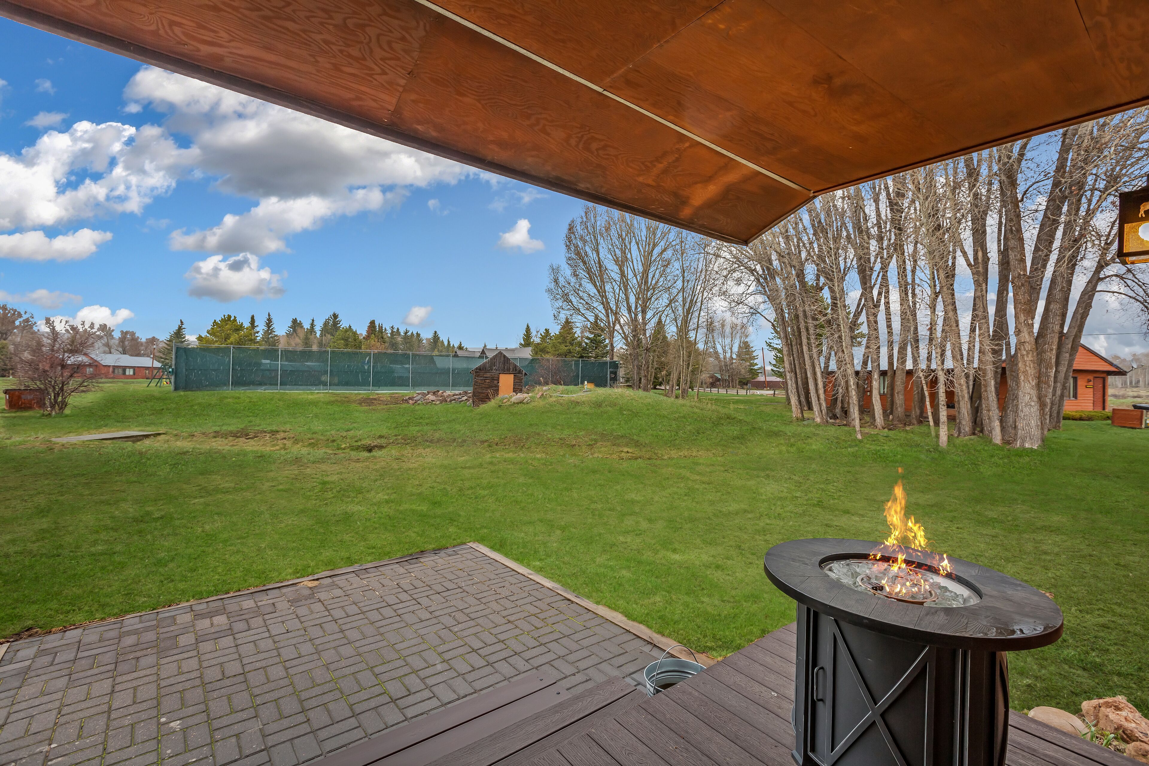 An outdoor deck with a fire pit, surrounded by a grassy yard and trees.