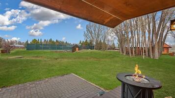 An outdoor deck with a fire pit, surrounded by a grassy yard and trees.