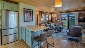 A modern kitchen with a stainless steel refrigerator, a wooden island with bar stools, and a cozy seating area with a leather couch and a coffee table.