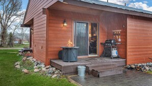 A wooden cabin with a deck, a fire pit, and a grill.