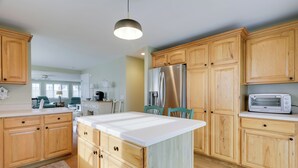 A kitchen with wooden cabinets, a stainless steel refrigerator, a microwave, and a large island with a white countertop. - Westerly Retreat ~ 1/4 Mi to Private Beach! (Westerly)