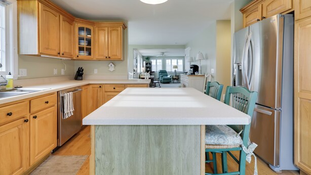 A modern kitchen with wooden cabinets, a stainless steel refrigerator, and a central island with chairs. - Westerly Retreat ~ 1/4 Mi to Private Beach! (Westerly)