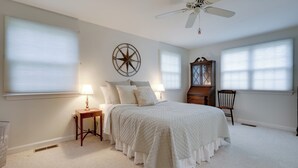 A bedroom with a bed, two bedside tables, a wooden chair, a ceiling fan, and a large window with blinds. - Westerly Retreat ~ 1/4 Mi to Private Beach! (Westerly)
