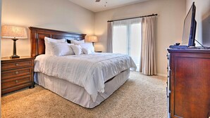 A bedroom with a bed, nightstands, a desk, a ceiling fan, and a window with curtains.