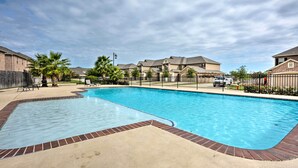 A swimming pool with a brick border, surrounded by a fence and palm trees.