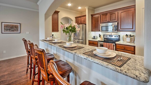 A kitchen with a long island, wooden chairs, a refrigerator, a microwave, and a sink.