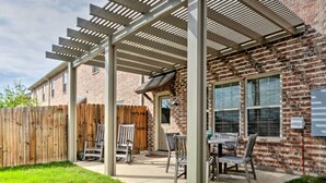 A patio area with a pergola, outdoor seating, and a brick house.