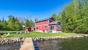 A red two-story house with a dock extending into a lake, surrounded by greenery and trees. - Spacious Lakeside Family Home on Big Bearskin Lake (Harshaw)