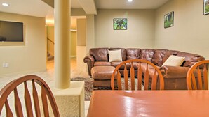 A living room with a brown leather sofa, wooden chairs, a dining table, and a TV mounted on the wall. - CO Springs Apartment < 6 Mi to Garden of the Gods! (Colorado Springs)