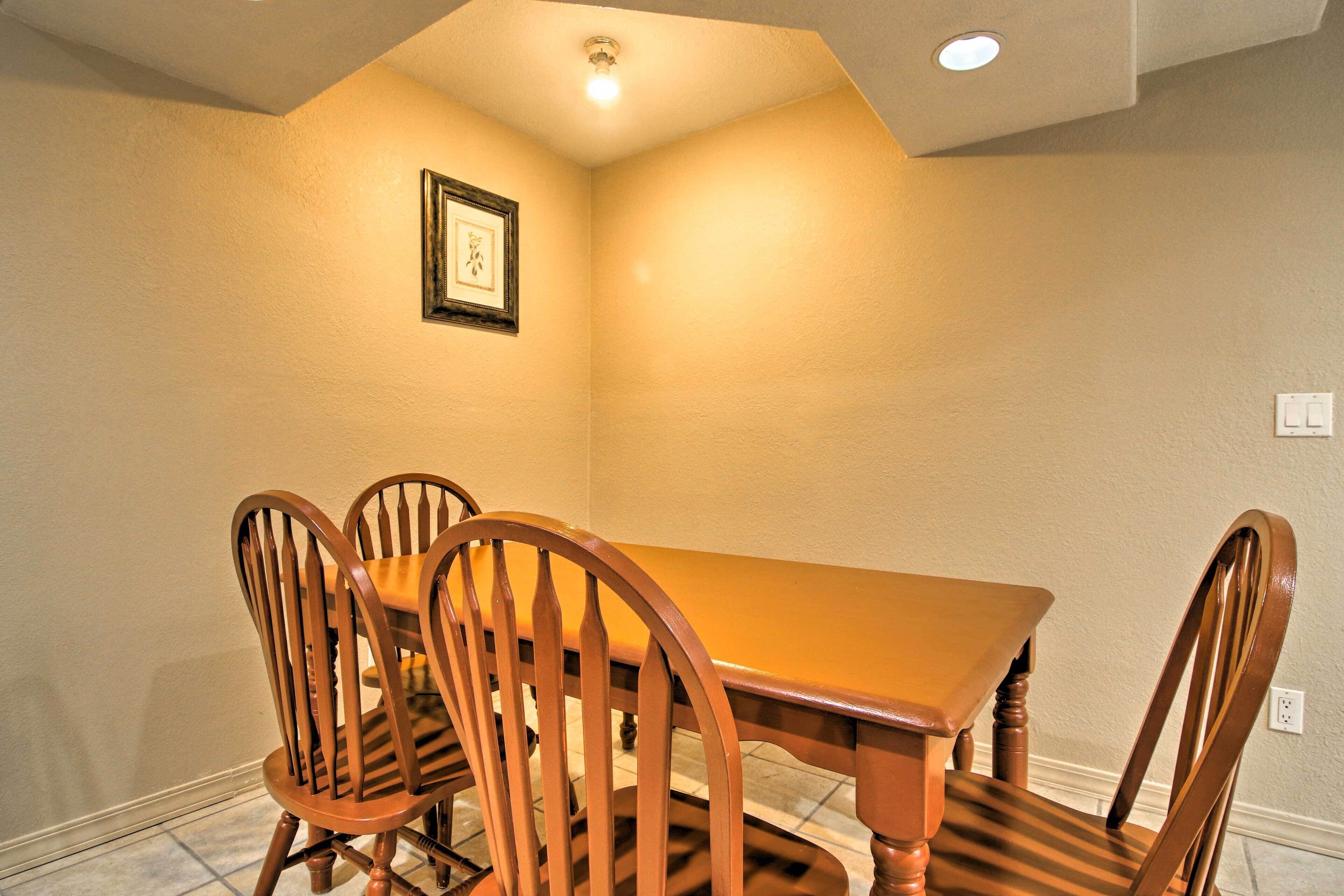 Un comedor con una mesa de madera y cuatro sillas, un cuadro en la pared y una lámpara de techo.