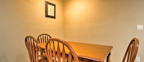 Un comedor con una mesa de madera y cuatro sillas, un cuadro en la pared y una lámpara de techo.