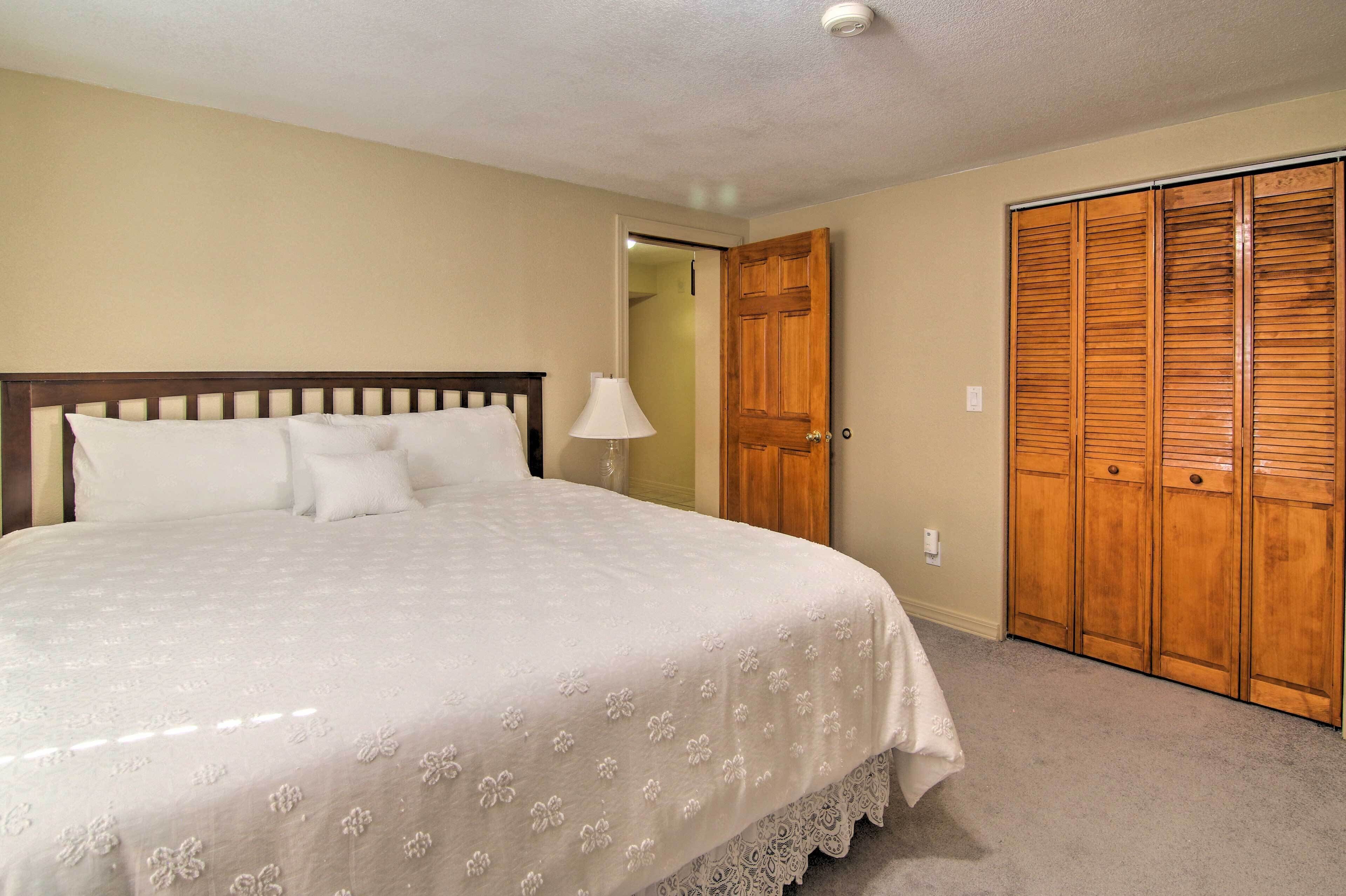 A bedroom with a large bed, a wooden wardrobe, and a door leading to another room.