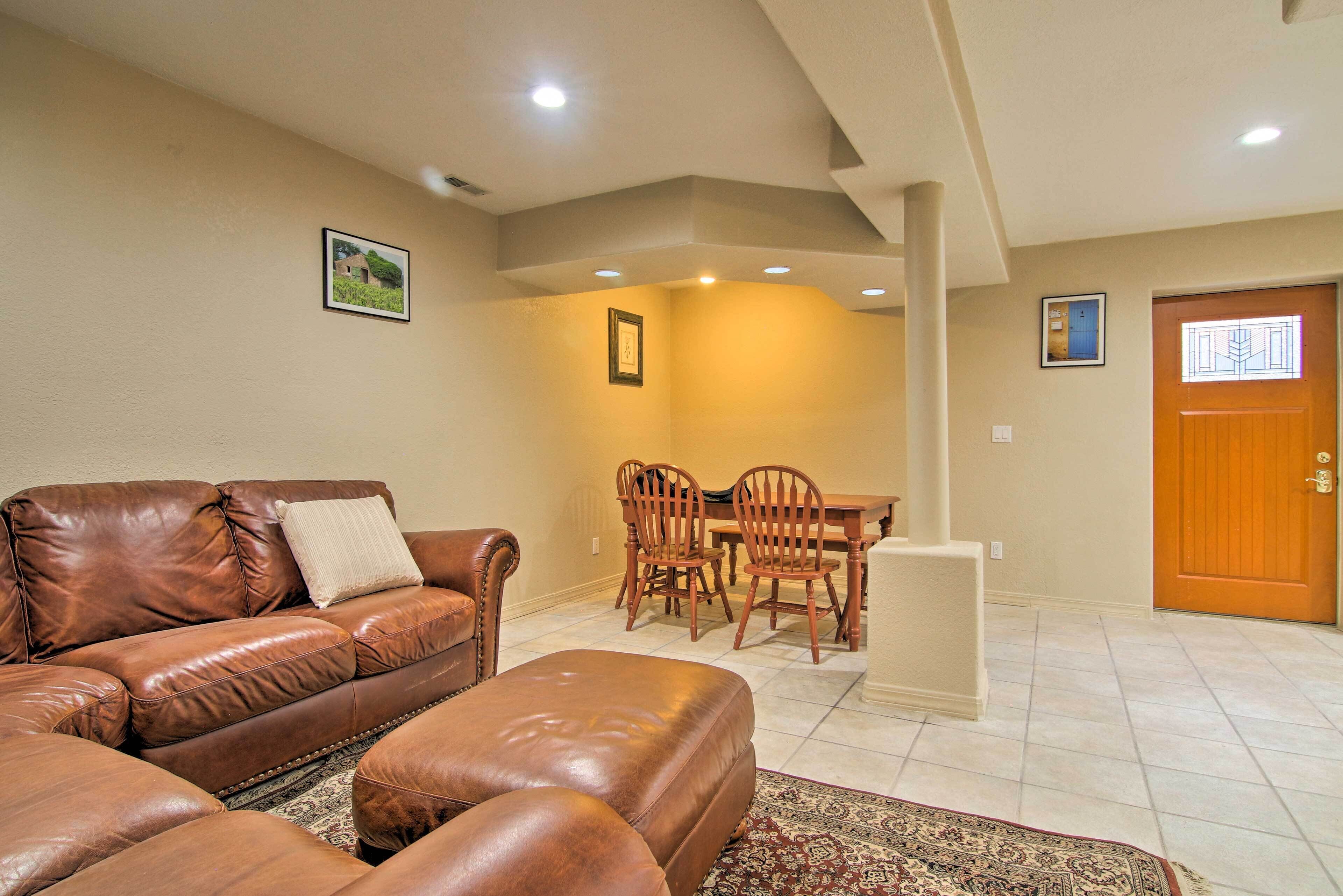 A living room with a brown leather sofa, a matching ottoman, and a dining area with wooden chairs and a table.