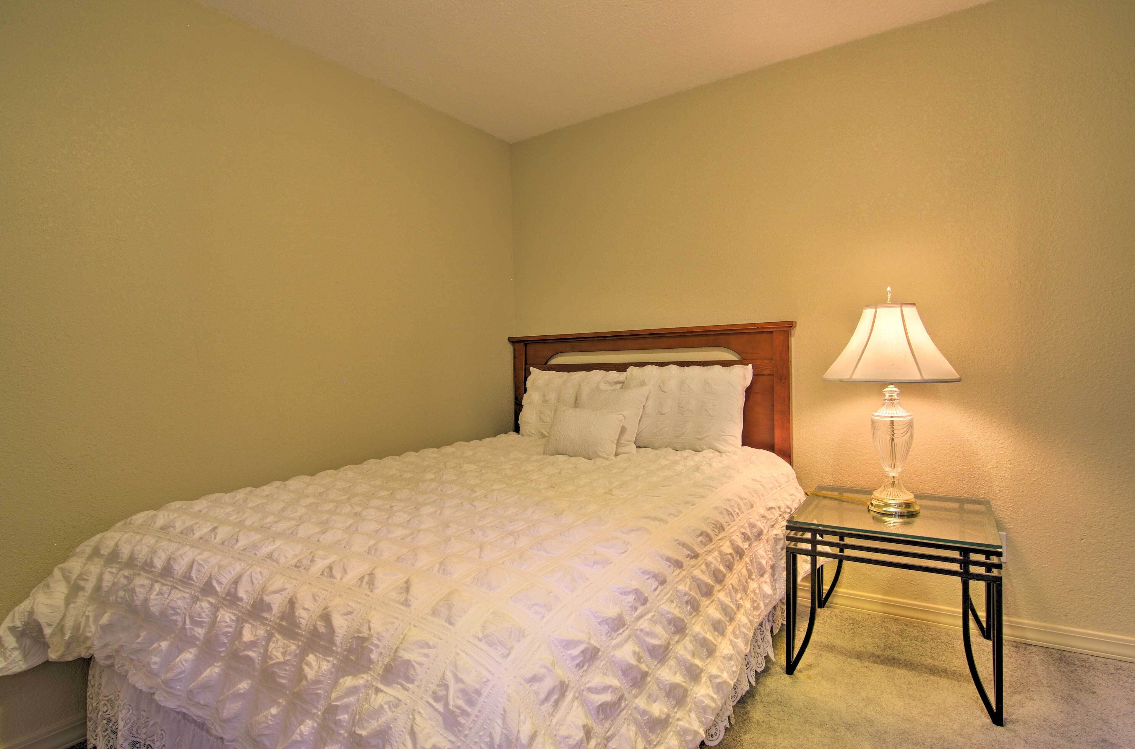 A bedroom with a bed, a bedside table with a lamp, and a plain wall.
