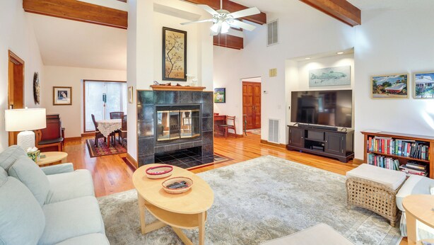 A spacious living room with a fireplace, wooden beams, a ceiling fan, and a television. - Spacious Kiawah Island Home w/ Deck, Walk to Beach (Kiawah Island)