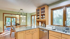 A kitchen with wooden cabinets, granite countertops, a dishwasher, and a window with a view of trees. - Spacious Kiawah Island Home w/ Deck, Walk to Beach (Kiawah Island)